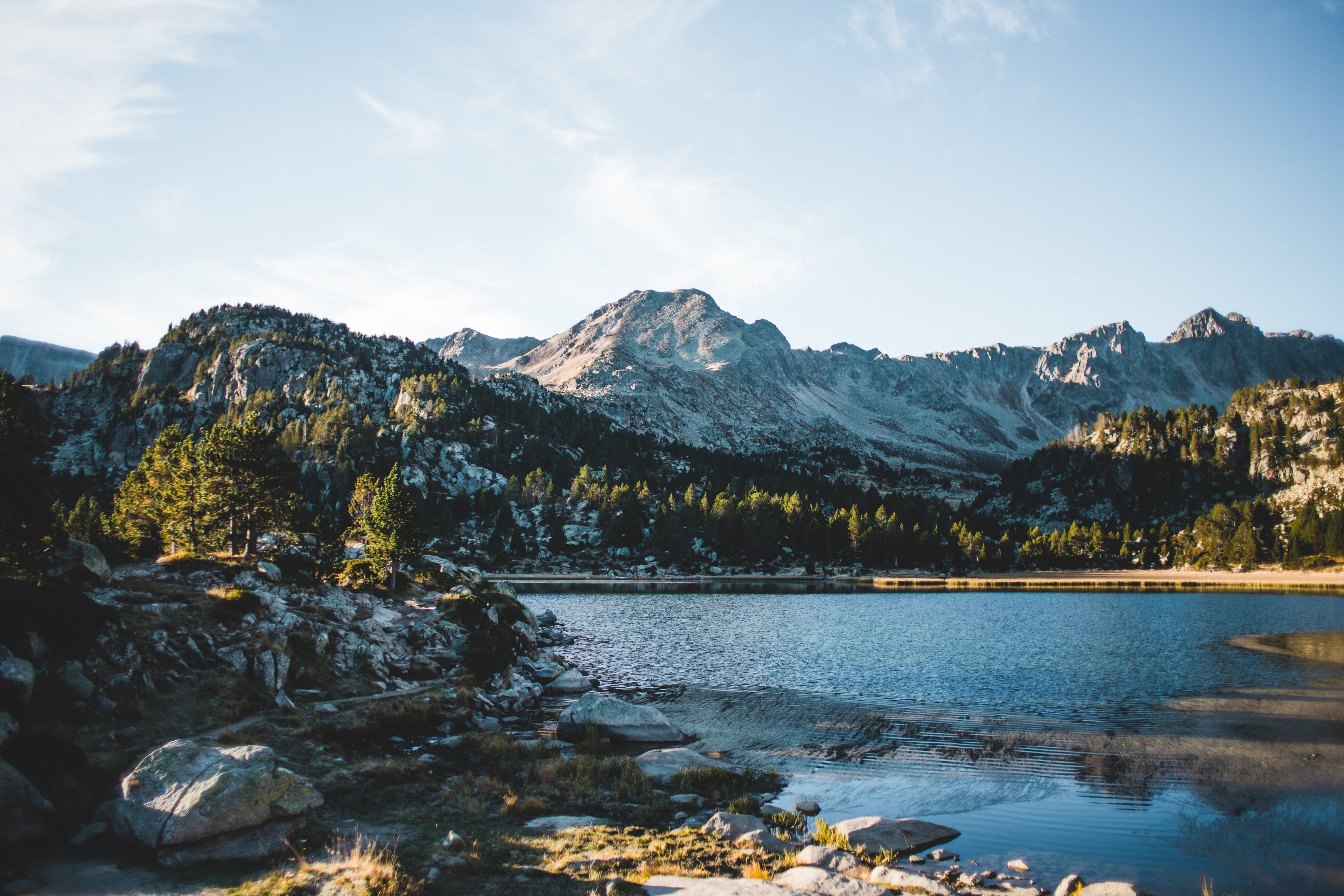 Mountain lake surrounded by trees and rocky terrain under a clear blue sky.
